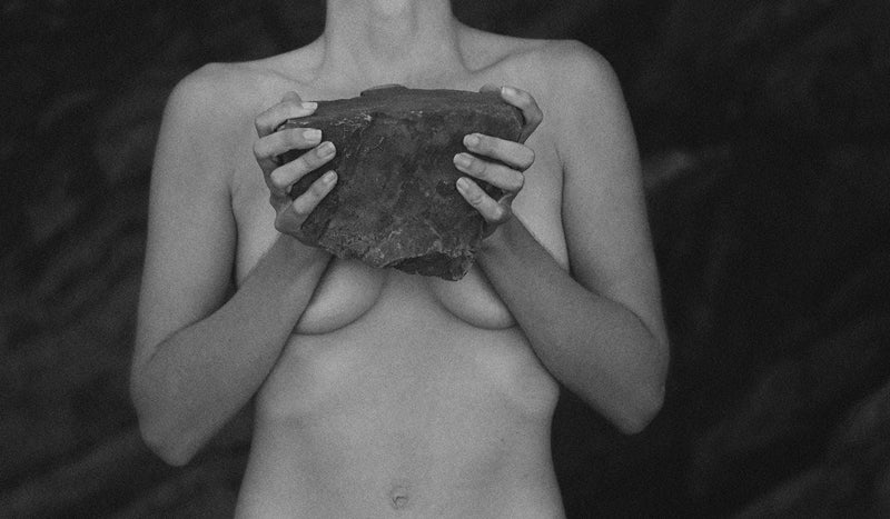 Image of naked woman holding natural rock covering her breasts